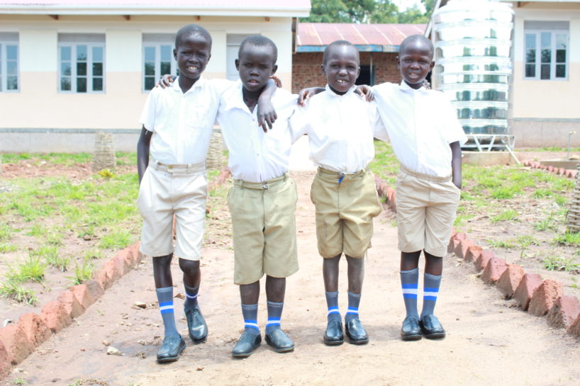 Four young boys at school in Uganda show of their new shoes