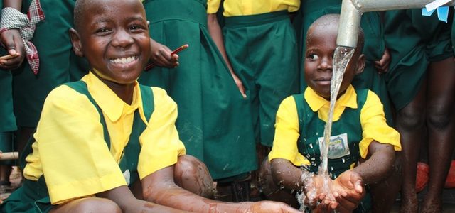 Two Happy Students In Uganda Smiling At Clean Water Well