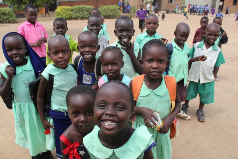 A group of young students in Uganda with green uniforms are smiling