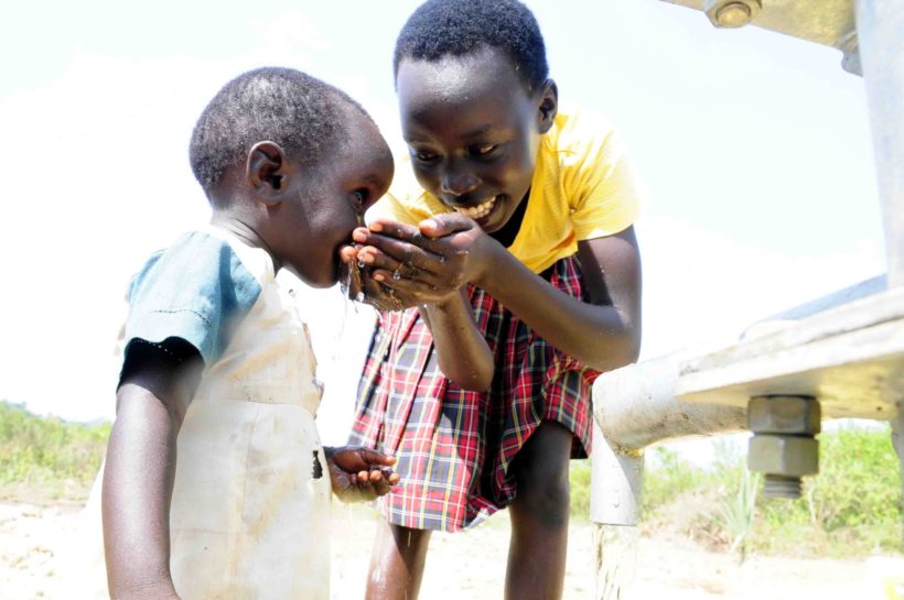 Older child in Uganda helps younger child take a sip of clean water