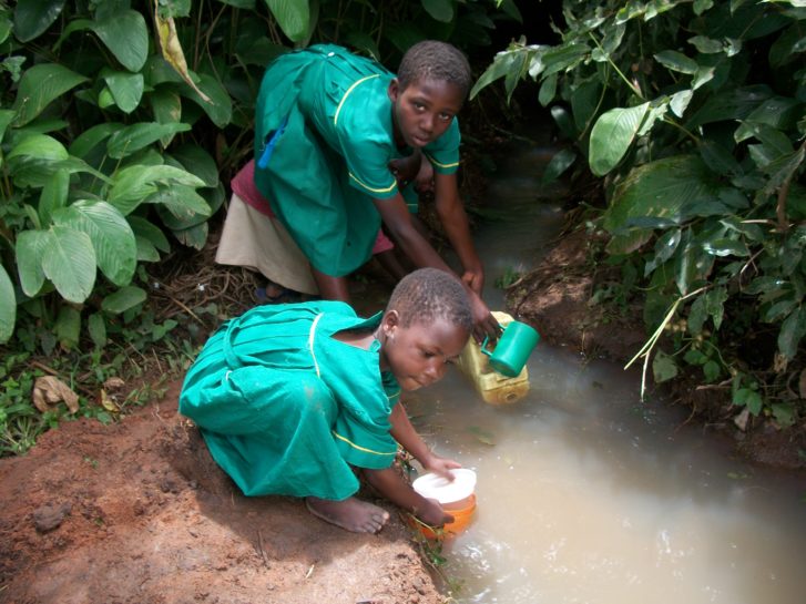 Two small girls fetch water from a dirty stream in Uganda