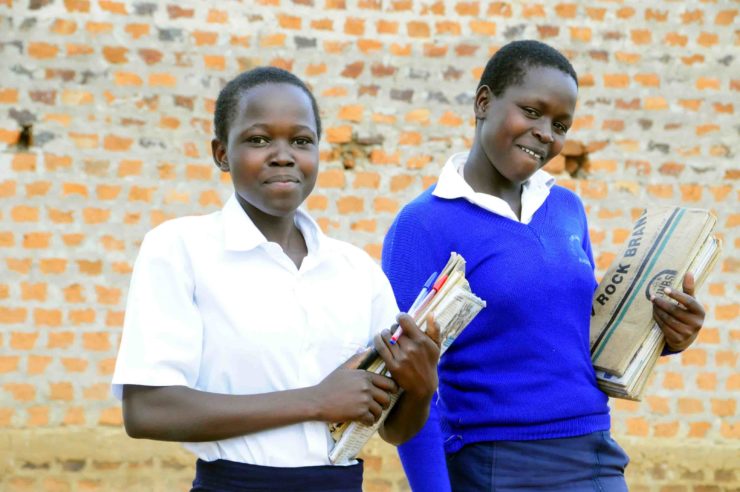 Two teenage female students with their books smiling in front of their school in Uganda