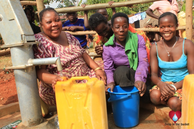 CoWomen smiling while collecting water at the Custom Corner community borehole in Gulu, Uganda. The well was recently drilled by Drop in the Bucket