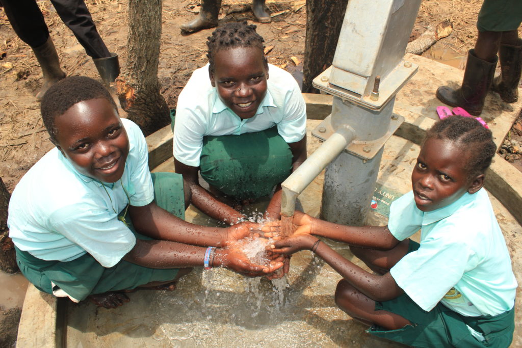 Three girls collecting clean water from the well at Wii-Aceng Primary School in Omoro, Uganda, drilled by Drop in the Bucket.