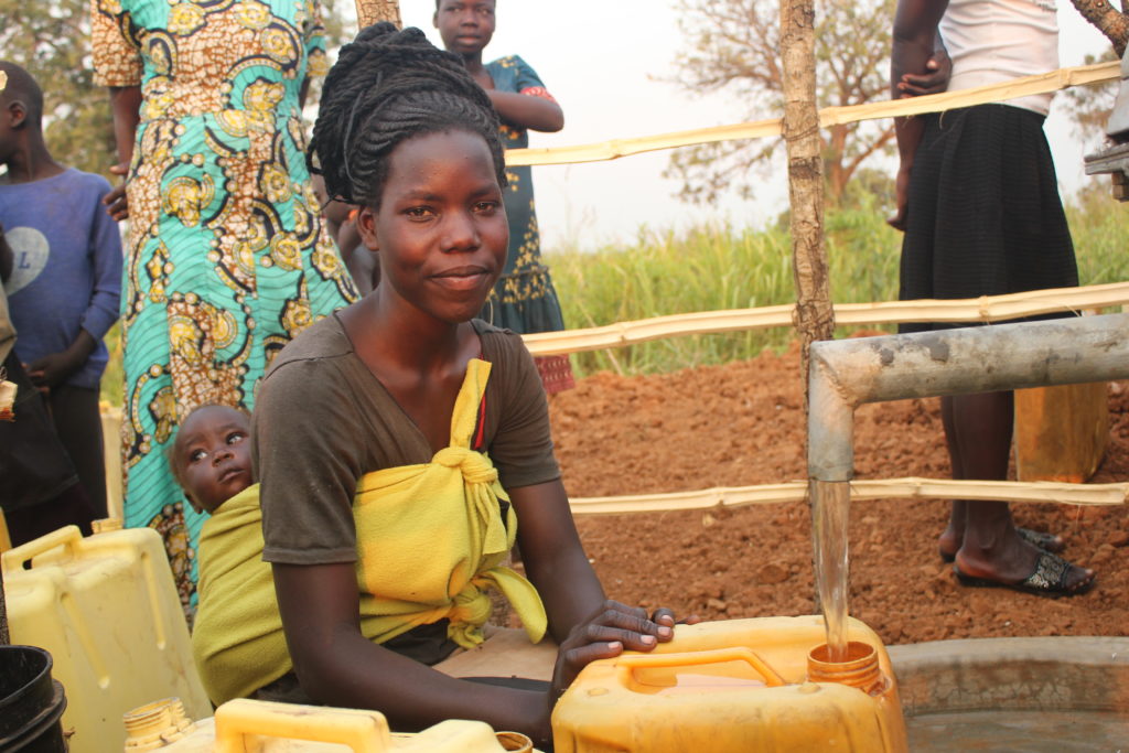 Mother with a baby on her back collecting clean water from the Pakuma community borehole well in Amuru, Uganda, drilled by Drop in the Bucket in November 2021.