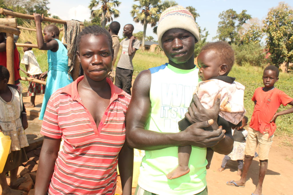 Two parents holding their baby standing by a water well drilled by the Los Angeles based water charity Drop in the Bucket for Kati-Kati West village in Gulu, Uganda