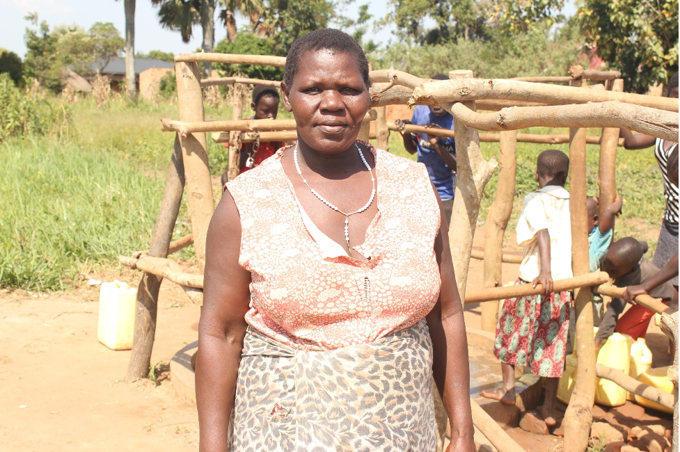 Akot Rose Ajok stands by the new well drilled by Drop in the Bucket in Kati Kati West