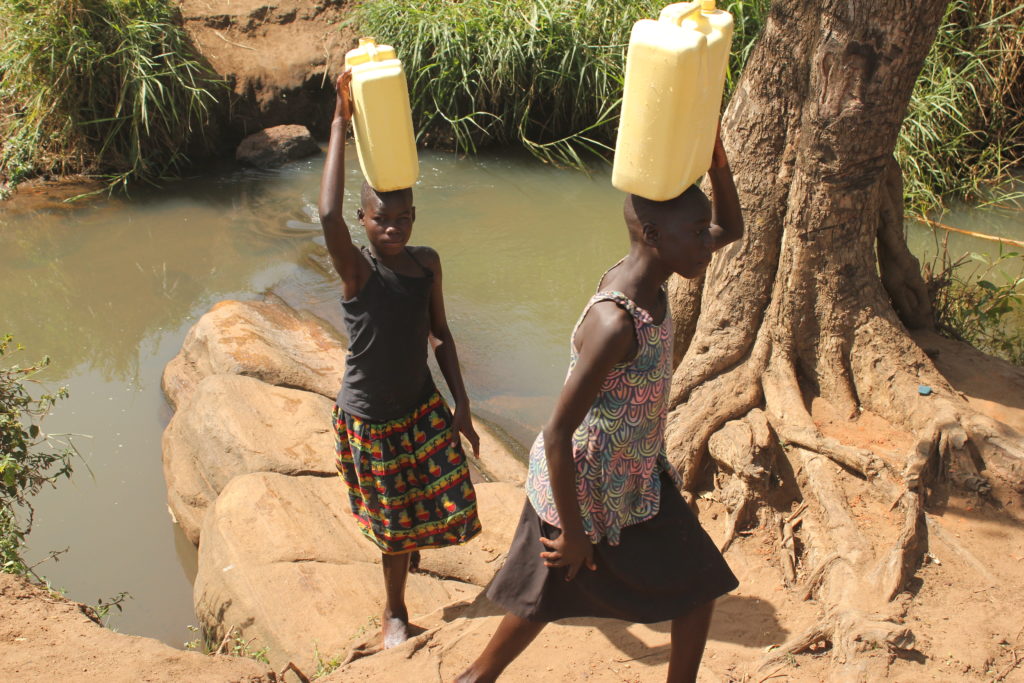 Two girls walking away from the old waterhole at Ngom Rom village in Gulu, Uganda. This was the village's only water source before Drop in the Bucket drilled a well there.