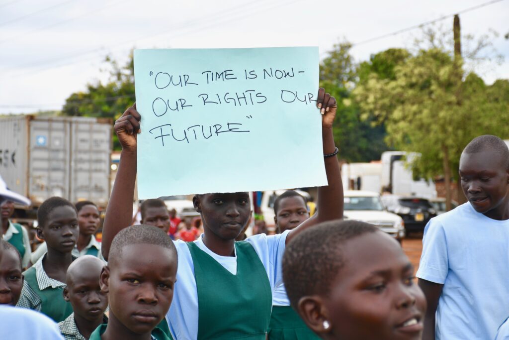A girl in Nimble South Sudan holds a sign with the words "Our time is now- our rights our future at the International Day of the Girl Child celebration 2023 sponsored by Drop in the Bucket