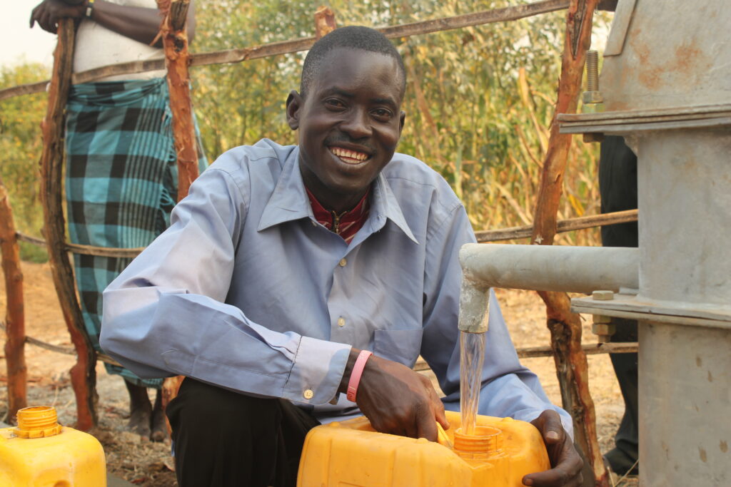 Okwera Julius from the Opam Okidi village in Amuru, Uganda smiles as he gets clean water from the well drilled by Drop in the Bucket.