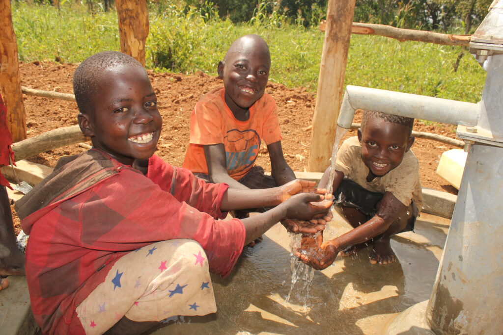 Three young boys collecting clean water from the new well drilled for Lamdogi village, Omoro, Uganda, by Drop in the Bucket.