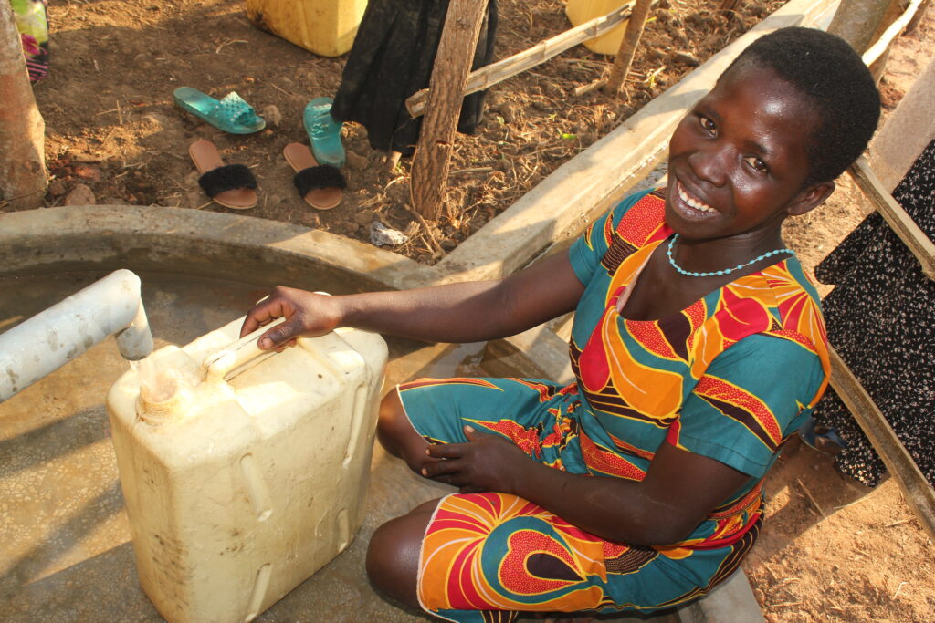 A woman collecting clean water from the newly drilled well in Akecha B village, Omoro, Uganda, by Drop in the Bucket.