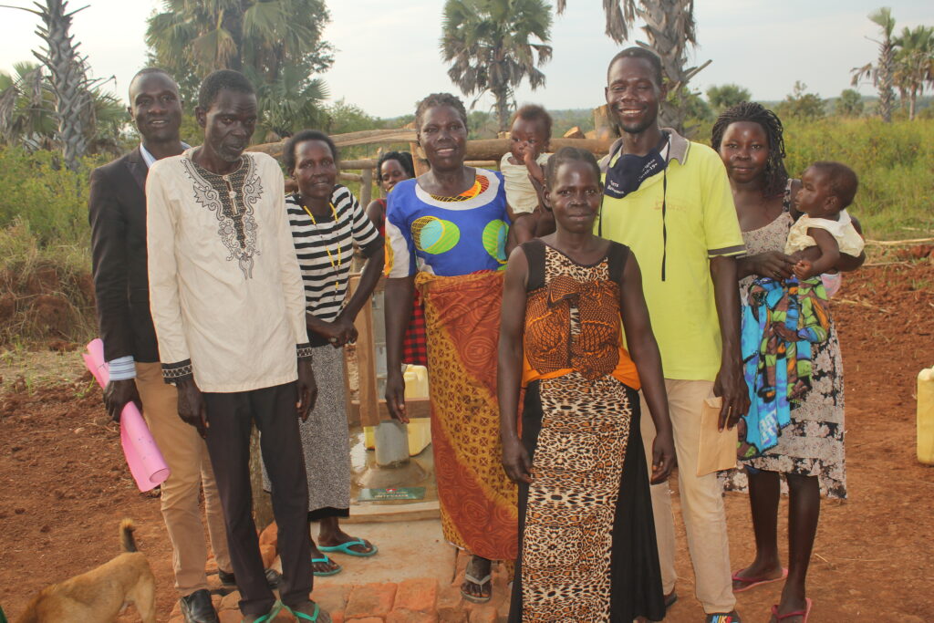 Community stakeholders from Apolioywe Otura Oloya village, Uganda, stand in front of the well drilled by Drop in the Bucket.