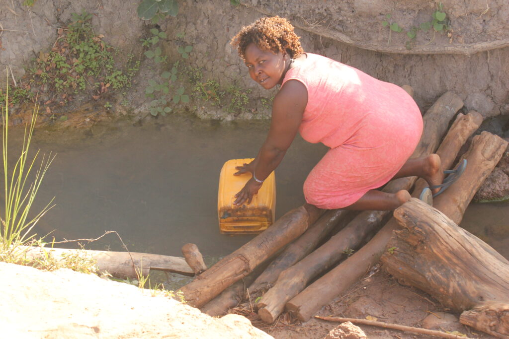 A woman collecting water from the previous water source in Pudyek village.