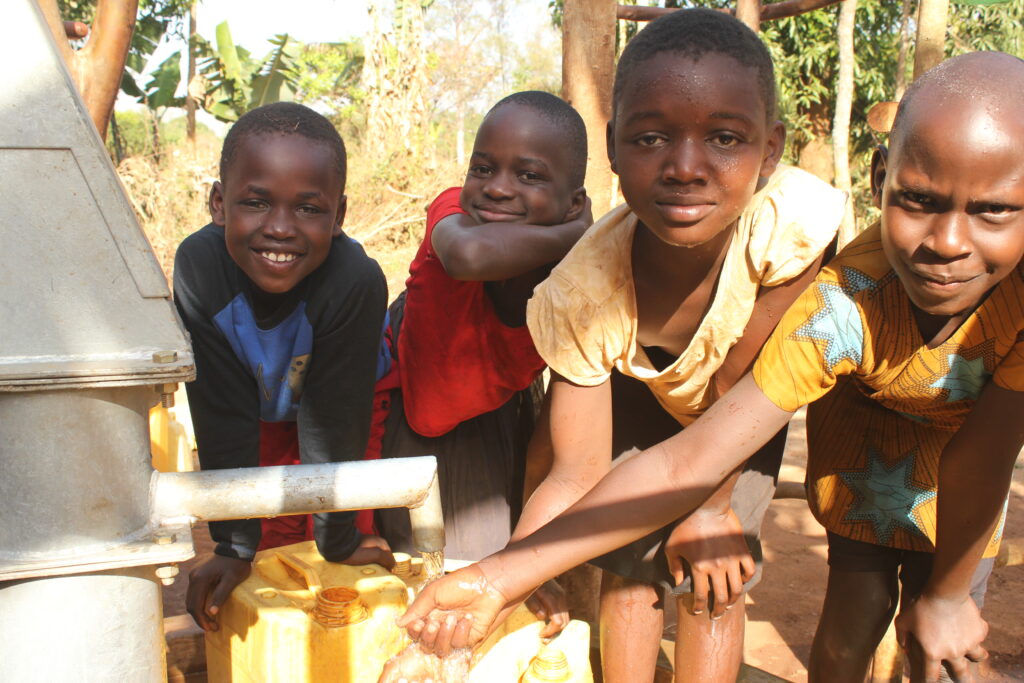 Four children collecting clean water from the new well in Pudyek village, Gulu, Uganda, drilled by Drop in the Bucket.