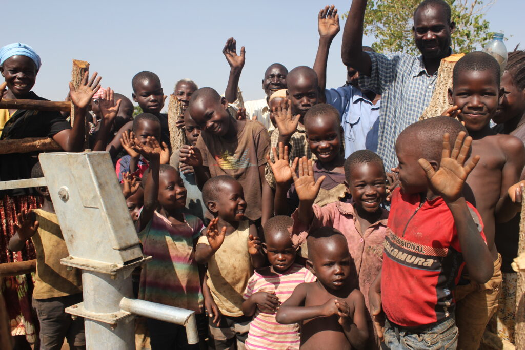 Children from Ngom Rom village wave and smile by the new well drilled by Drop in the Bucket in Uganda.