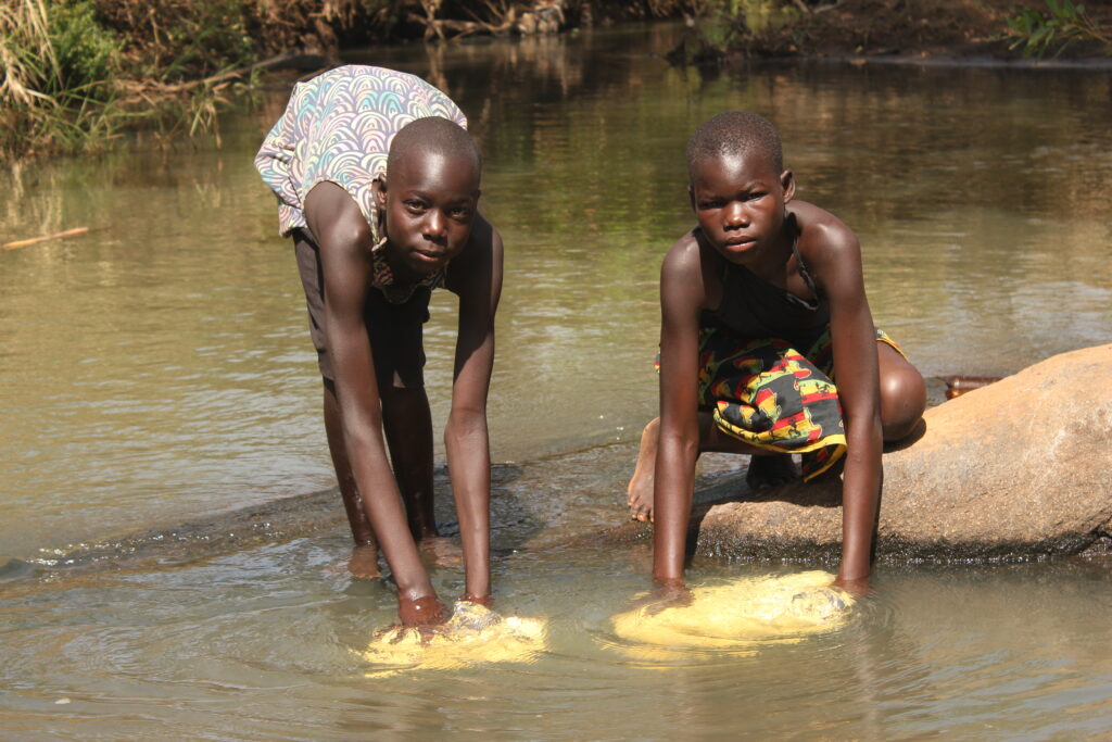 Two girls collecting water from a stream in Ngom Rom Uganda