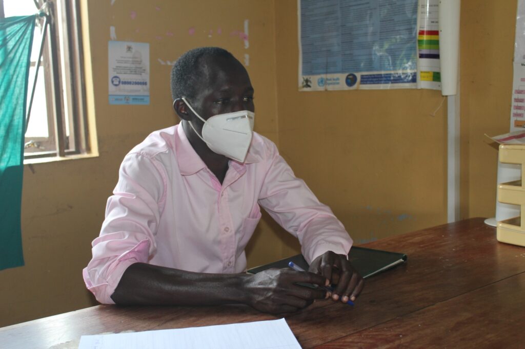 Ojok Isaac, the nursing officer of Awere HC III sits at his desk wearing a mask. This photo was taken while Uganda was under a strict lockdown during the covid 19 pandemic.