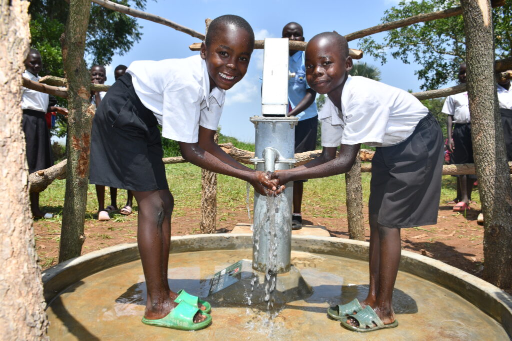 Two students get clean water from the new well in Paminyai sub-county in Uganda. The well was drilled by US based water charity Drop in the Bucket. 