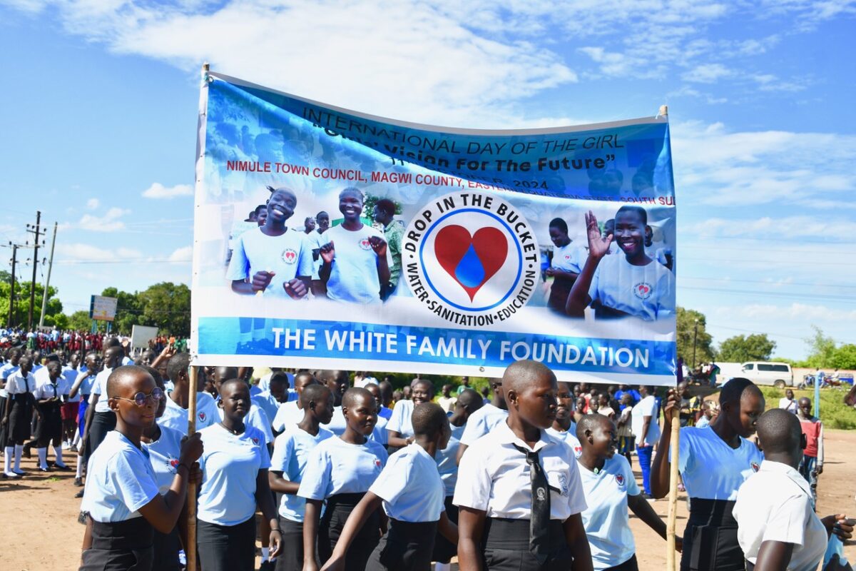 Female students in Nimule South Sudan marching as part of the International Day of the Girl celebrations holding a banner for event sponsor Drop in the Bucket.