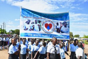 Female students in Nimule South Sudan marching as part of the International Day of the Girl celebrations holding a banner for event sponsor Drop in the Bucket.