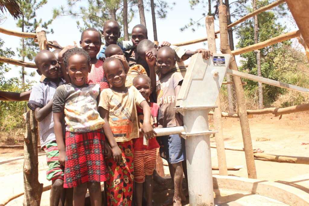 Children from Amoyokomo Primary School in Gulu, Uganda, stand near the new well drilled by Drop in the Bucket, providing safe water to the school.