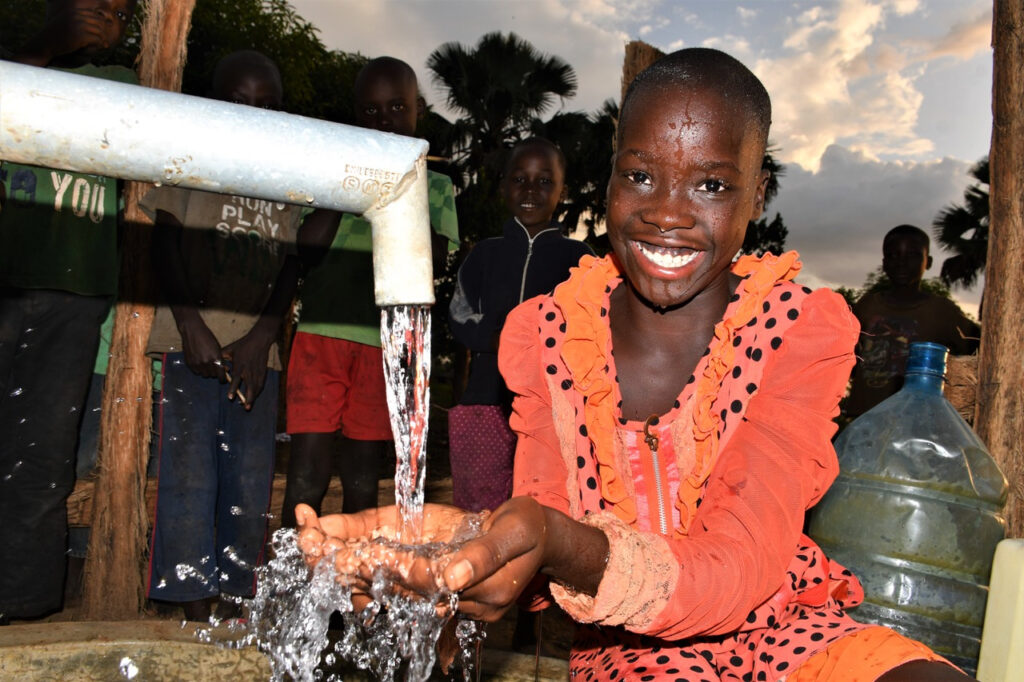 A young girl collecting clean water from a newly drilled well in Obia West, Uganda, providing safe water access for the community.