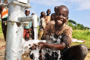 A young boy smiles while collecting clean water from a well in Uganda, representing the life-changing impact of clean water access.