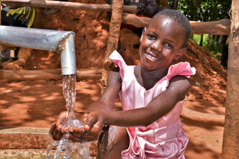 Smiling young girl drinking clean water from the new well at Twon Okun village, Gulu, Uganda