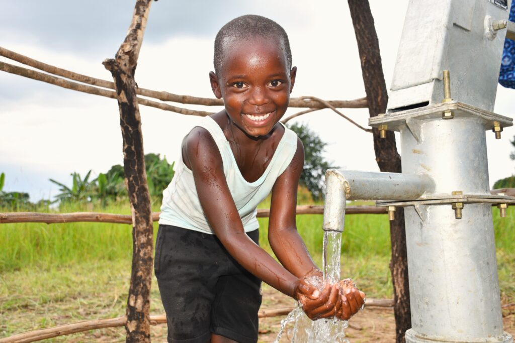 Young boy getting clean water from a well drilled by Africa water charity Drop in the Bucket in Nwoya District, Uganda.