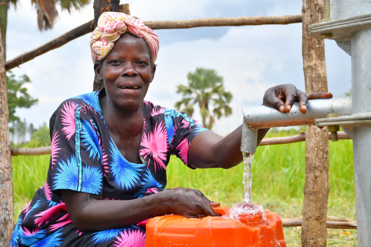 A mother fills a large container with clean water from a well drilled by water Africa charity Drop in the Bucket in Nwoya District, Uganda.