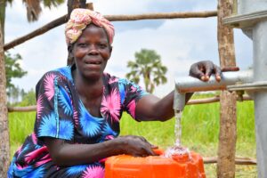 A mother fills a large container with clean water from a well drilled by water Africa charity Drop in the Bucket in Nwoya District, Uganda.