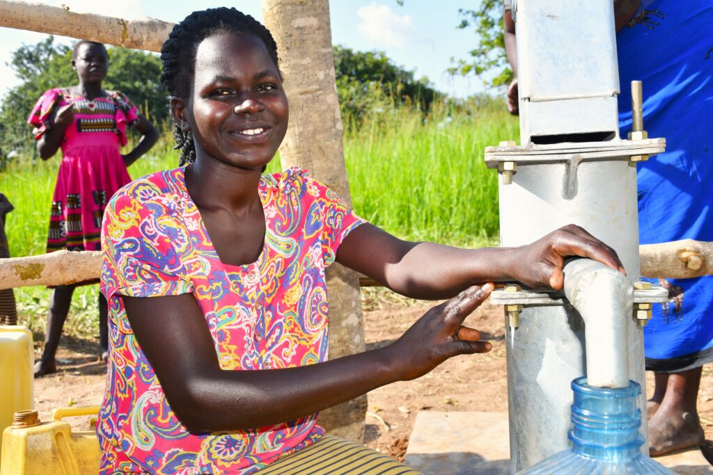 Ugandan woman filling a large container with clean water from a well drilled by water Africa charity Drop in the Bucket in Nwoya District, Uganda.