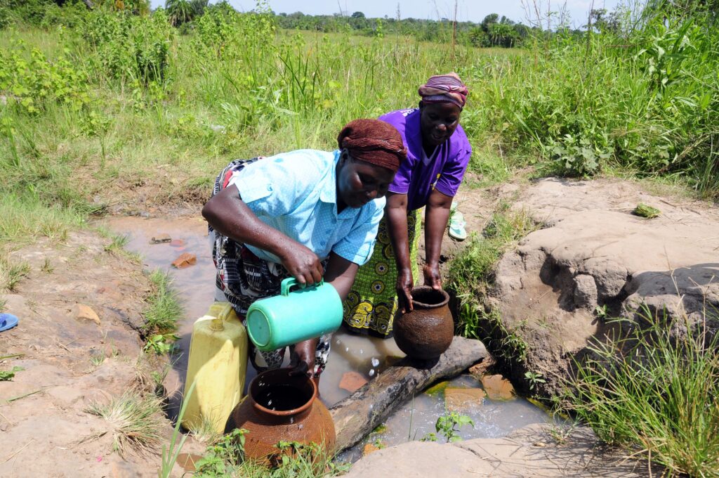 Two women collecting water from a traditional well in Uganda