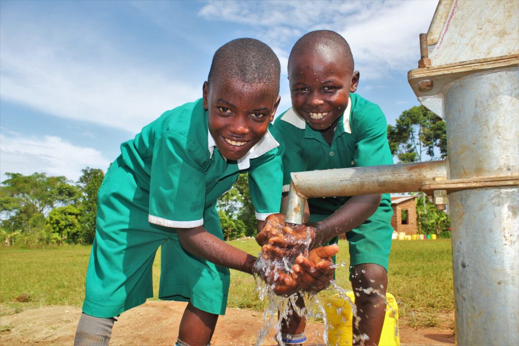 Two boys getting clean water from a recently drilled well at St Kiziti Primary School in Iganaga, Uganda