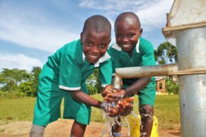 Two boys getting clean water from a recently drilled well at St Kiziti Primary School in Iganaga, Uganda