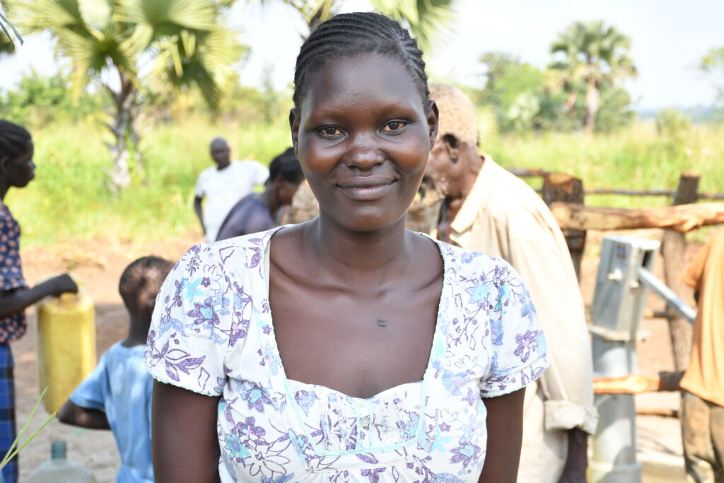 Adong Mary Mercy stands near a new borehole well in Paminano-A, Uganda, installed to provide safe, reliable water for the village.