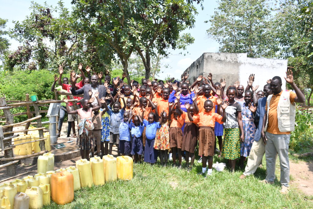 The staff and pupils of the Covenant Nursery and primary school in Okura, Uganda stand by the new well drilled by Africa water charity Drop in the Bucket