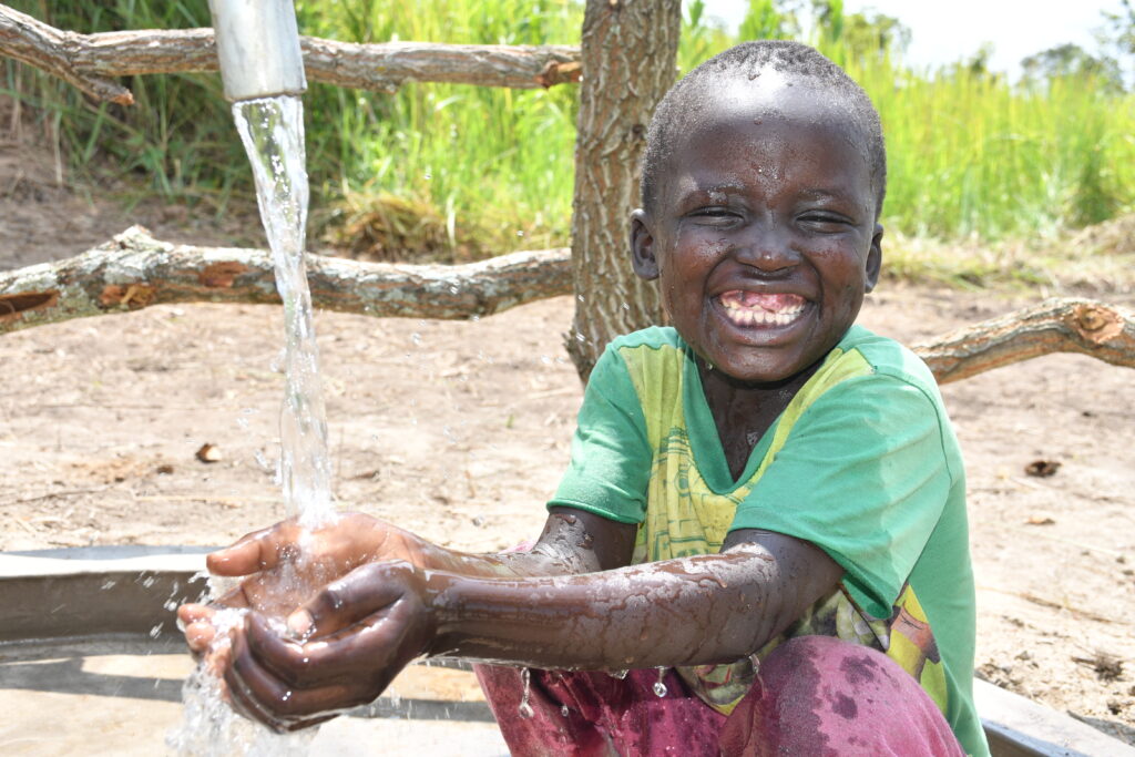 Young child getting clean water from the new well in Lakwatomer village in northern Uganda