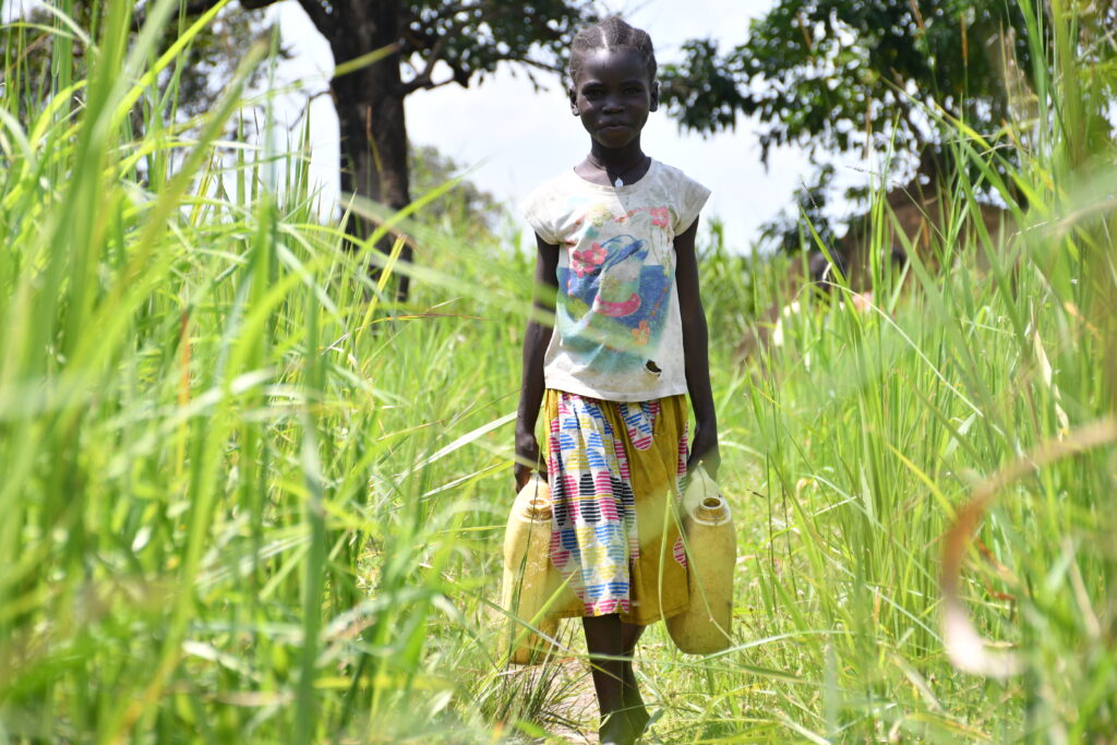 Young girl from Lakwatomer village in northern Uganda walks through long grass to get from the old unsafe water source to her home in the village