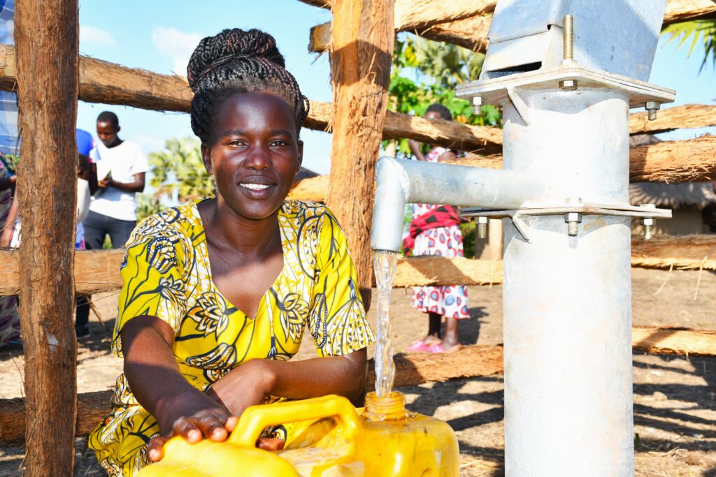 A woman wearing a traditional Ugandan yellow dress gets clean water from a borehole in Awornyim Central village in Gulu, Uganda