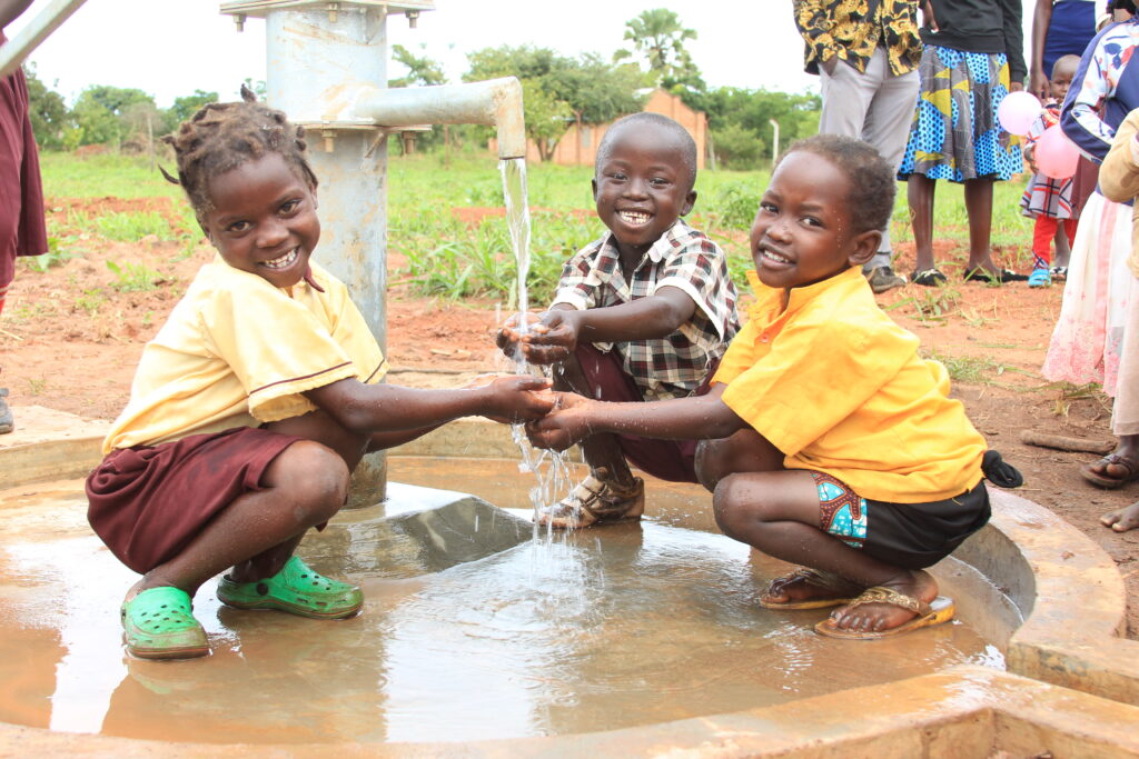 Three young children getting clean water from a water well in Lamin Ayila in Omoro, Uganda drilled by Drop in the Bucket.