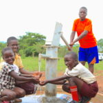 Four young children getting clean water from a water well in Lamin Ayila in Omoro, Uganda drilled by Drop in the Bucket.