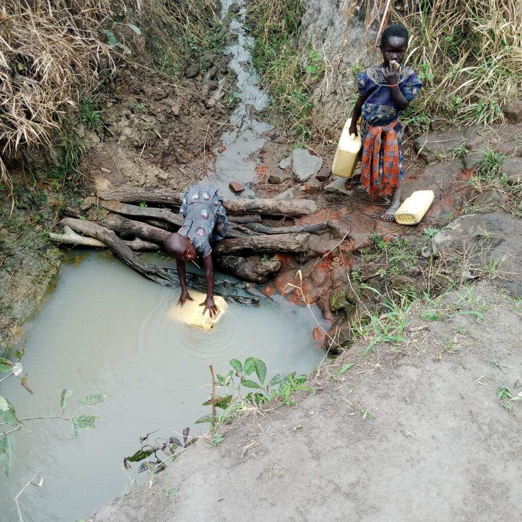 Two children getting dirty water from an unsafe source in Uganda. This photo in on a page that discusses causes of the water crisis in Africa