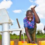 A woman from Tukupe community in Amuru, Uganda waves as she uses the new well drilled by Drop in the Bucket