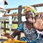 A woman from the Awornyim central community in Gulu, Uganda  waves as she gets safe water from a new borehole 